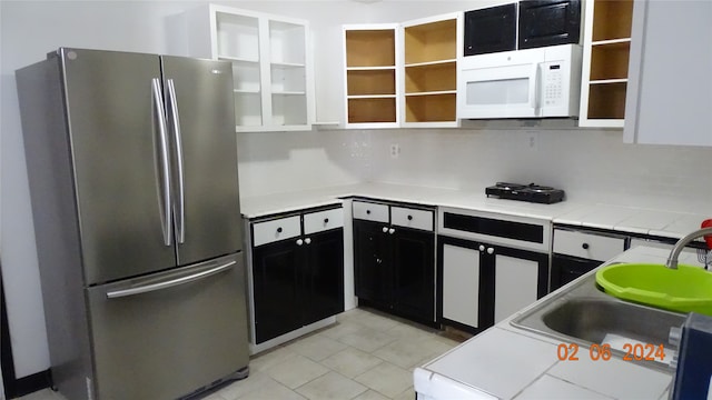 kitchen featuring stainless steel refrigerator, light stone counters, light tile floors, sink, and white cabinets