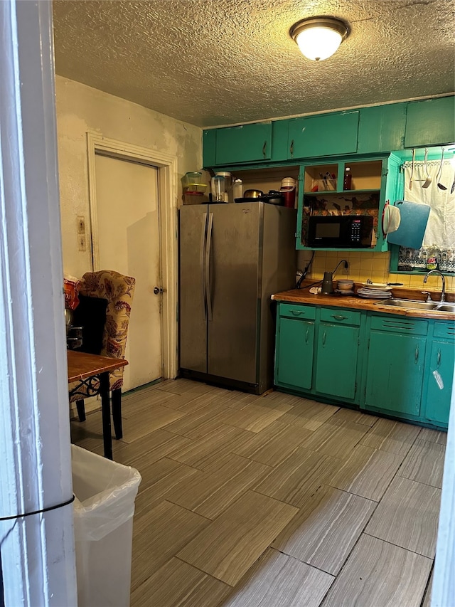 kitchen featuring green cabinets, a textured ceiling, stainless steel fridge, and sink