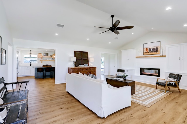 living room featuring ceiling fan, light wood-type flooring, and vaulted ceiling