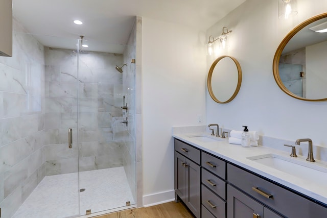 bathroom with dual sinks, a shower with door, hardwood / wood-style flooring, and vanity with extensive cabinet space