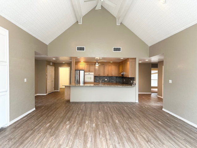 kitchen featuring ceiling fan, high vaulted ceiling, stainless steel fridge, kitchen peninsula, and dark stone countertops