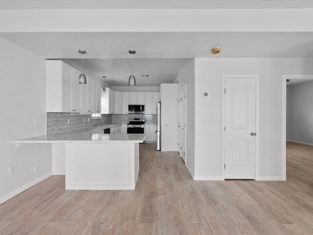 kitchen featuring backsplash, stainless steel appliances, kitchen peninsula, hanging light fixtures, and light hardwood / wood-style floors