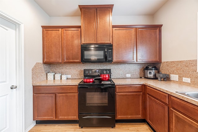 kitchen with backsplash, black appliances, and light wood-type flooring