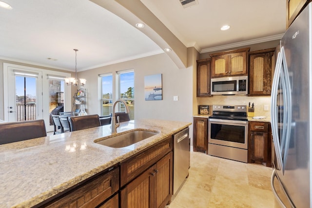 kitchen with sink, an inviting chandelier, light stone counters, decorative light fixtures, and stainless steel appliances