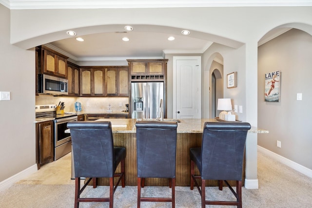 kitchen featuring a breakfast bar, appliances with stainless steel finishes, backsplash, light stone counters, and ornamental molding