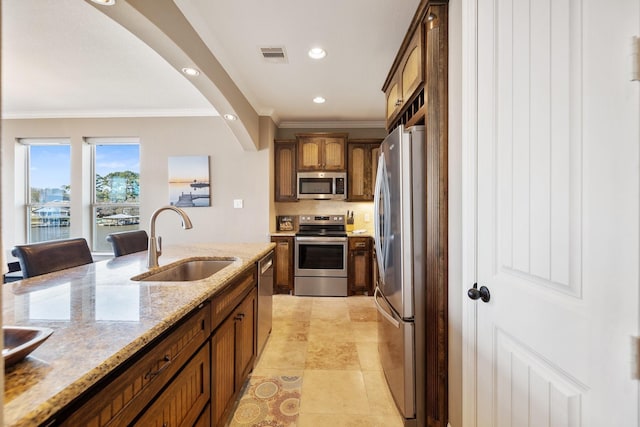 kitchen with sink, a breakfast bar, stainless steel appliances, ornamental molding, and light stone countertops