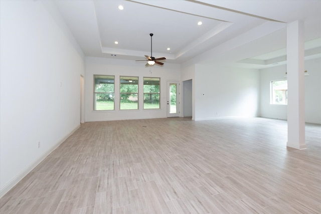 empty room featuring plenty of natural light, ceiling fan, a tray ceiling, and light hardwood / wood-style flooring