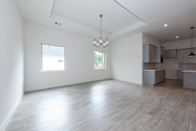 unfurnished living room featuring a raised ceiling, a notable chandelier, and light wood-type flooring