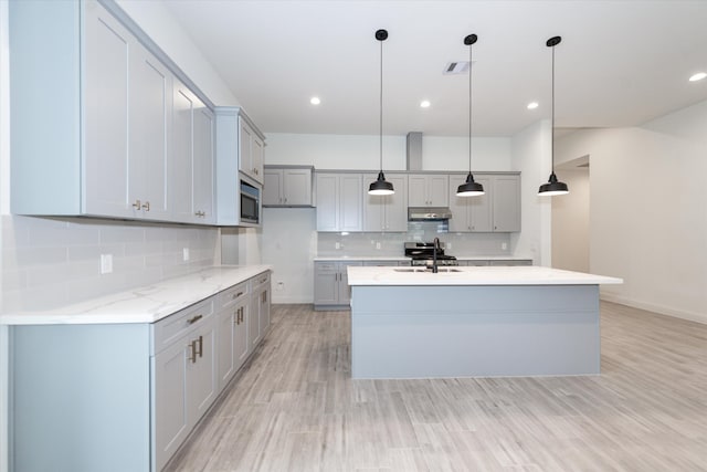 kitchen with appliances with stainless steel finishes, decorative light fixtures, tasteful backsplash, and a center island with sink