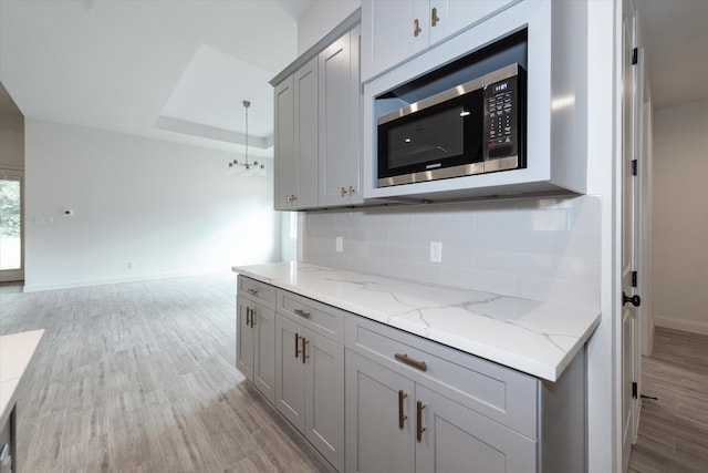 kitchen with gray cabinetry, stainless steel microwave, a tray ceiling, tasteful backsplash, and light wood-type flooring