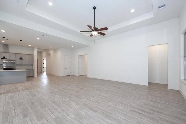 unfurnished living room featuring ceiling fan, a raised ceiling, and light hardwood / wood-style floors