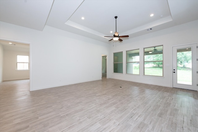 empty room with ceiling fan, a healthy amount of sunlight, light hardwood / wood-style floors, and a raised ceiling