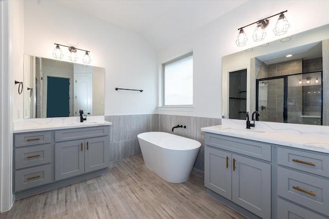 bathroom featuring tile walls, dual bowl vanity, a washtub, and vaulted ceiling