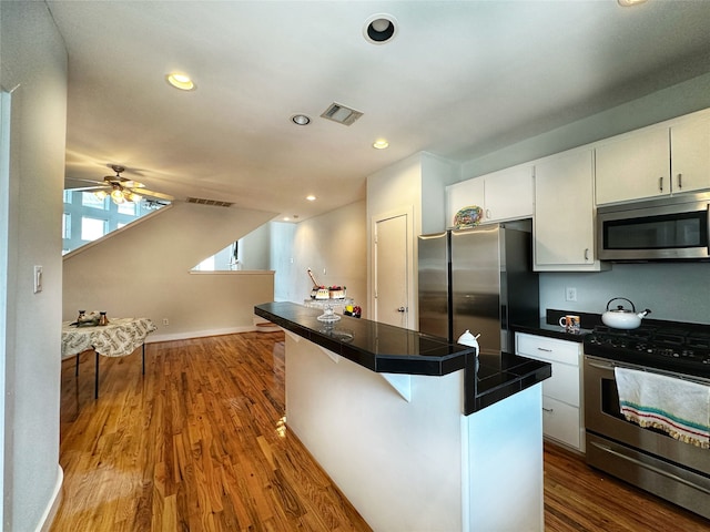 kitchen with white cabinets, ceiling fan, appliances with stainless steel finishes, wood-type flooring, and a kitchen bar