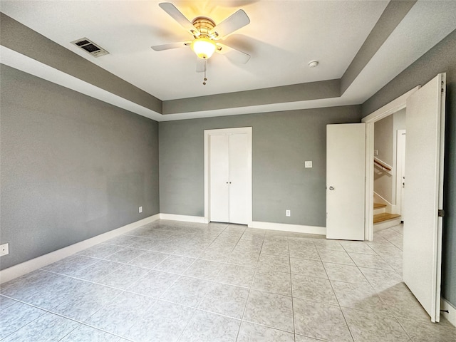 unfurnished bedroom with ceiling fan, a tray ceiling, a closet, and light tile patterned floors