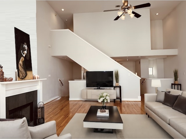 living room with hardwood / wood-style floors, a tiled fireplace, ceiling fan, and a towering ceiling