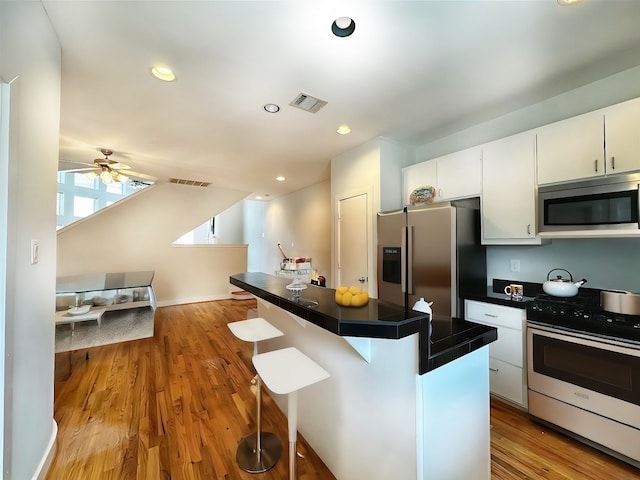 kitchen with white cabinets, ceiling fan, stainless steel appliances, light hardwood / wood-style floors, and a kitchen breakfast bar