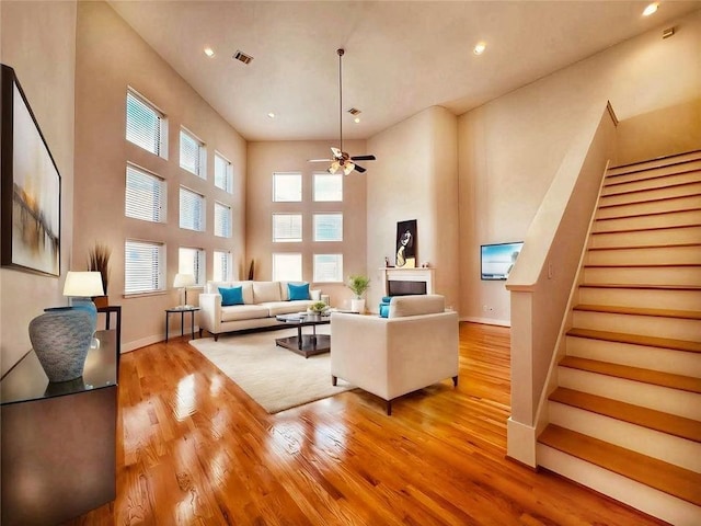 living room with a towering ceiling, light wood-type flooring, and ceiling fan