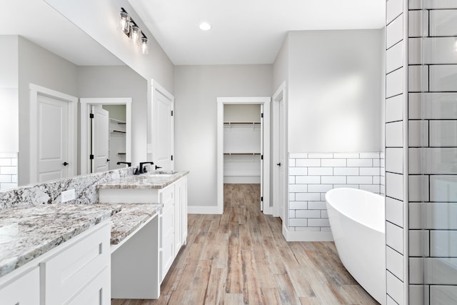 bathroom featuring hardwood / wood-style floors, tile walls, vanity, and a bath to relax in