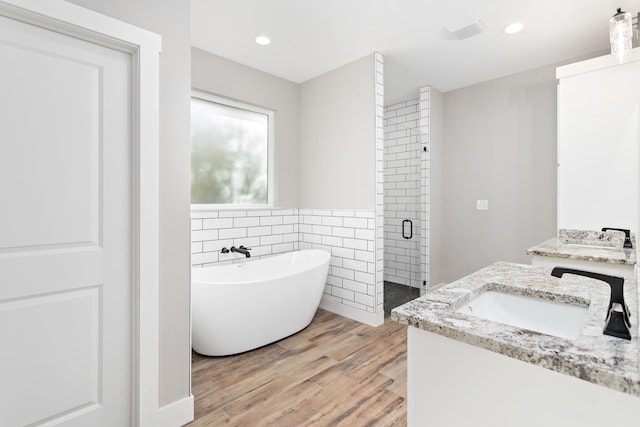 bathroom with wood-type flooring, plus walk in shower, vanity, and tile walls