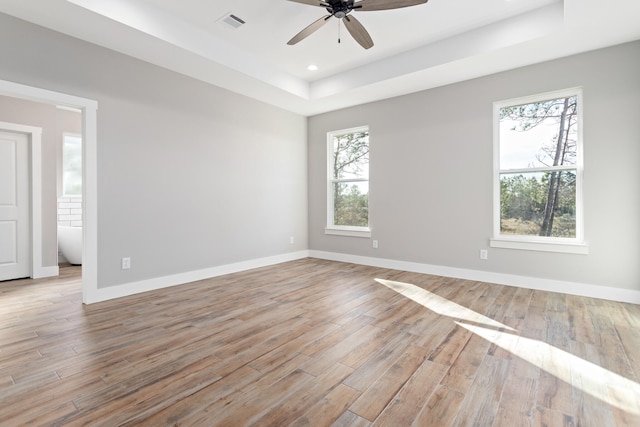 empty room featuring ceiling fan, a tray ceiling, and light hardwood / wood-style flooring