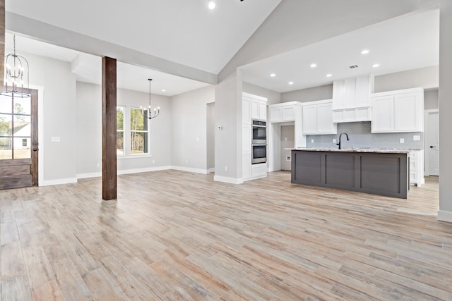 kitchen featuring white cabinets, tasteful backsplash, light wood-type flooring, and a kitchen island with sink