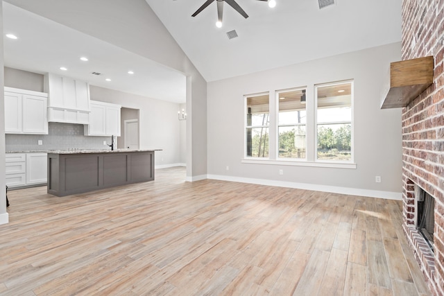 kitchen featuring ceiling fan, light hardwood / wood-style flooring, a fireplace, backsplash, and vaulted ceiling