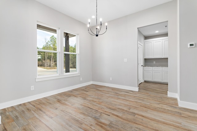 empty room with a chandelier, light hardwood / wood-style flooring, and a wealth of natural light