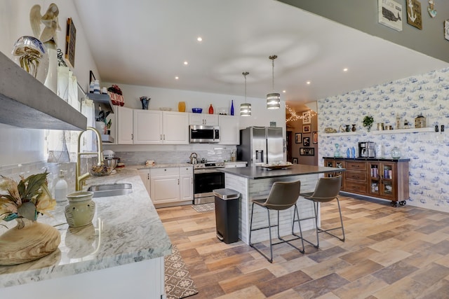 kitchen featuring appliances with stainless steel finishes, sink, a center island, white cabinetry, and decorative light fixtures