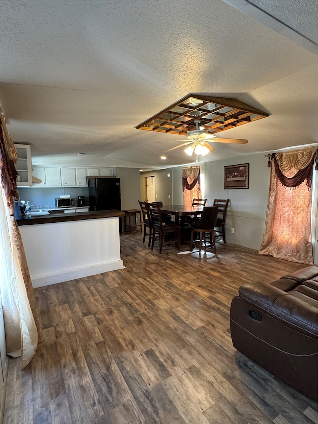 kitchen with dark wood-type flooring, white cabinetry, ceiling fan, and black fridge