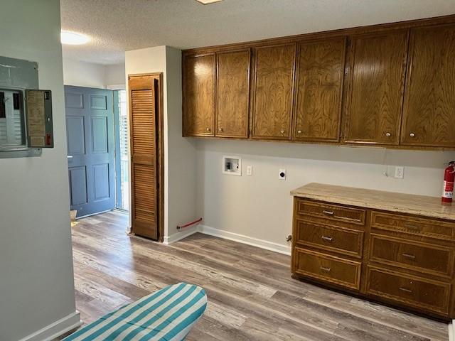 washroom with hookup for an electric dryer, a textured ceiling, light hardwood / wood-style flooring, cabinets, and hookup for a washing machine