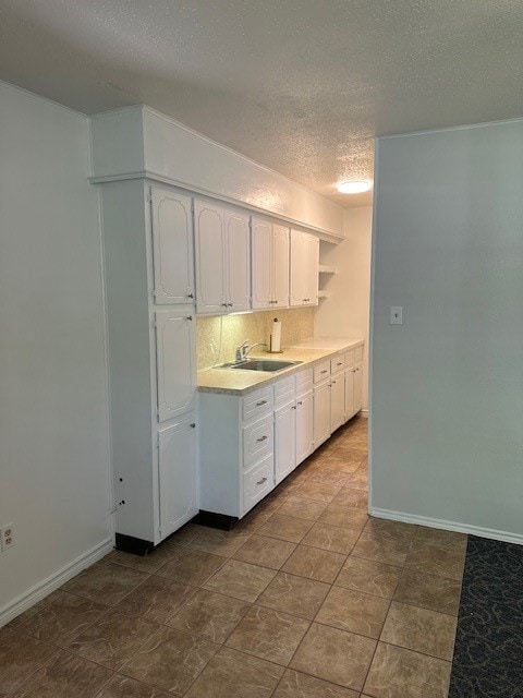 kitchen with sink, a textured ceiling, white cabinetry, tile patterned floors, and decorative backsplash