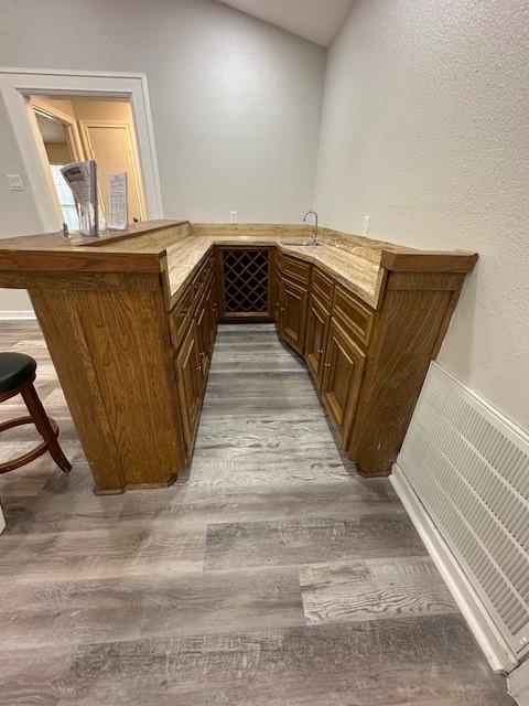 bar featuring light hardwood / wood-style floors, vaulted ceiling, and sink