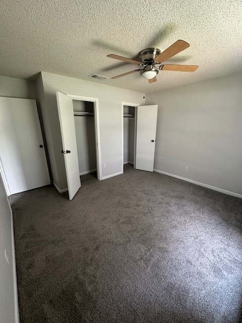 unfurnished bedroom with a textured ceiling, dark carpet, ceiling fan, and multiple closets