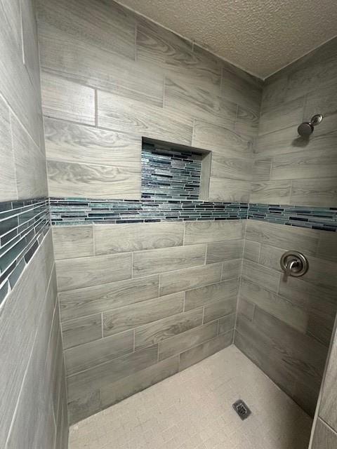 bathroom with a textured ceiling, tile walls, and tiled shower