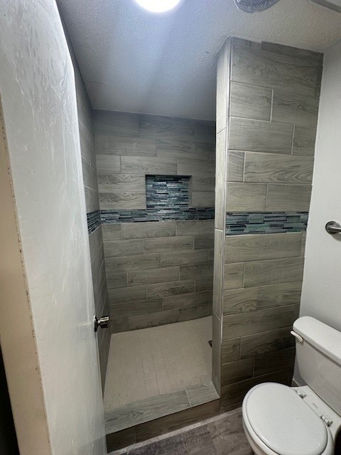 bathroom featuring a textured ceiling, a tile shower, toilet, and hardwood / wood-style flooring