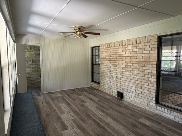 spare room featuring wooden walls, ceiling fan, brick wall, and dark hardwood / wood-style floors