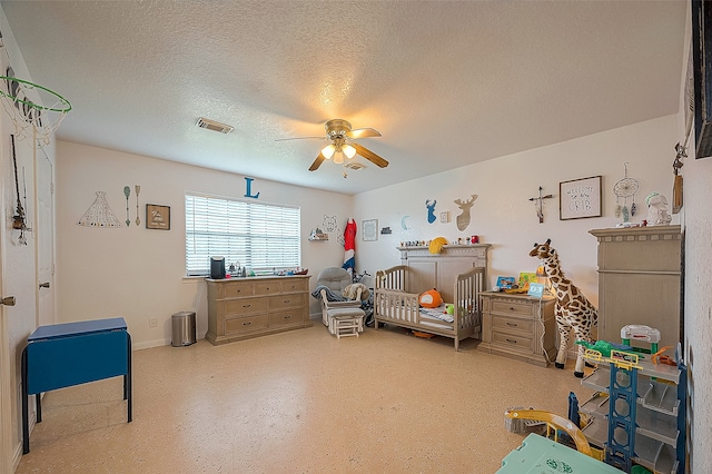 bedroom featuring a nursery area, ceiling fan, and a textured ceiling