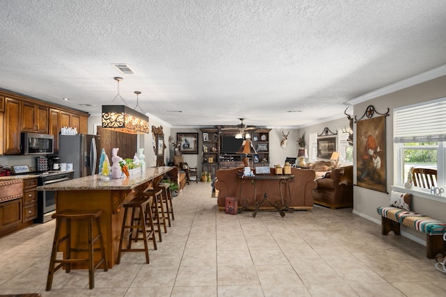 kitchen featuring appliances with stainless steel finishes, dark stone countertops, a kitchen bar, ceiling fan with notable chandelier, and a center island