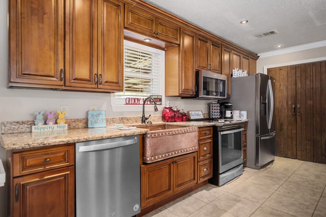 kitchen featuring light stone counters, ornamental molding, appliances with stainless steel finishes, light tile flooring, and a textured ceiling