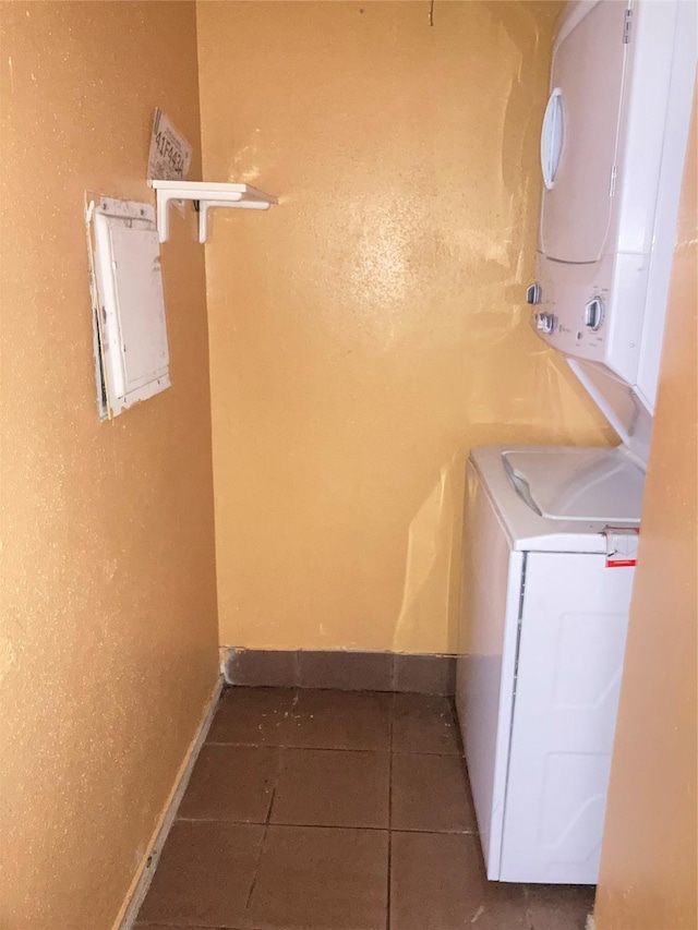 clothes washing area featuring electric panel, stacked washer and dryer, and dark tile patterned flooring