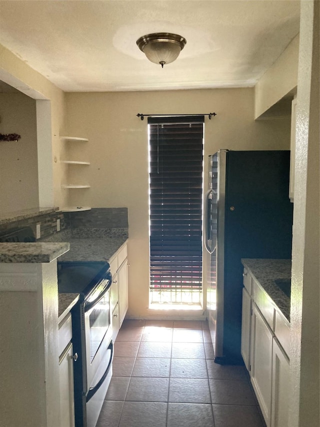 kitchen featuring electric stove, stainless steel fridge, white cabinets, and dark tile patterned flooring