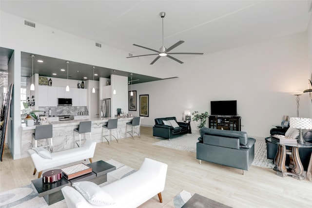 living room with light hardwood / wood-style floors, ceiling fan, and a high ceiling