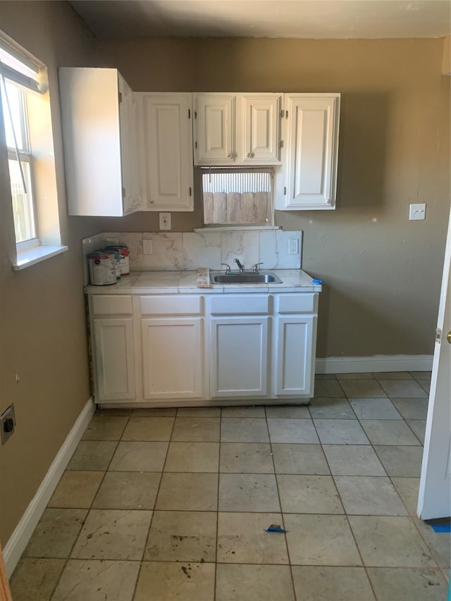 kitchen featuring sink, backsplash, light tile floors, and white cabinets