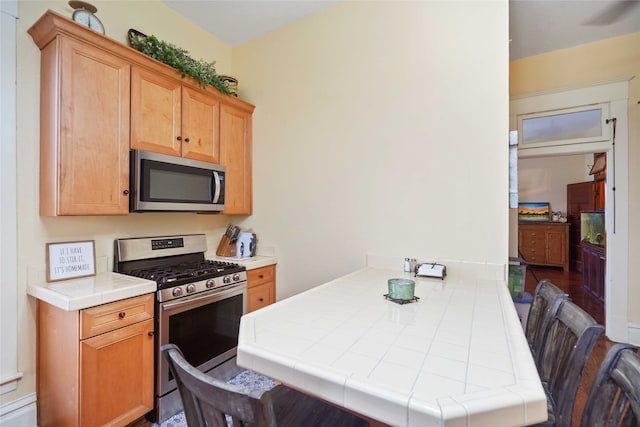 kitchen with appliances with stainless steel finishes, hardwood / wood-style flooring, kitchen peninsula, and tile countertops