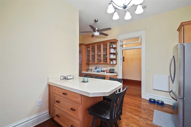 kitchen with stainless steel fridge, kitchen peninsula, a kitchen breakfast bar, tile counters, and hardwood / wood-style floors