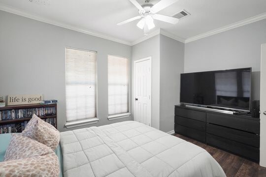 bedroom with multiple windows, wood-type flooring, ceiling fan, and ornamental molding