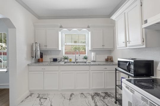 kitchen featuring stove, sink, white cabinetry, and a wealth of natural light