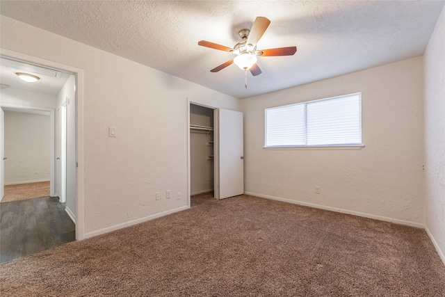 unfurnished bedroom featuring dark carpet, a textured ceiling, a closet, and ceiling fan