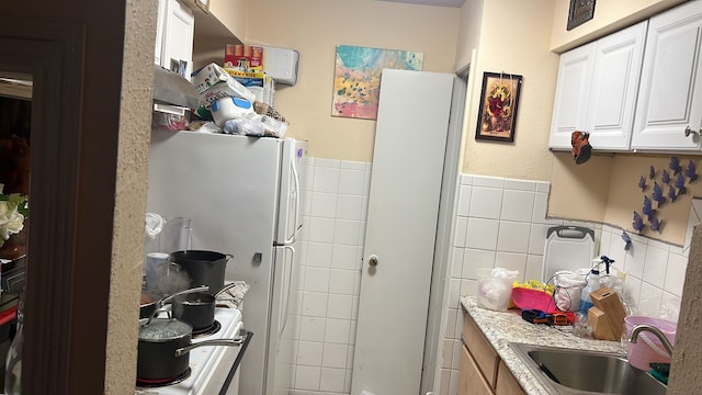 kitchen featuring white cabinetry, white fridge, sink, and tile walls